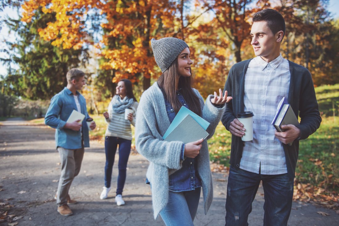 Studenci z książkami i kawą na jesiennym spacerze w parku